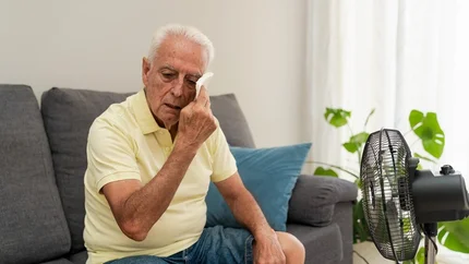oudere man dept zijn gezicht zittend op de bank met ventilator op zich gericht