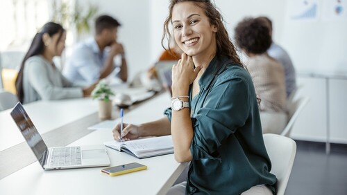 jonge vrouw achter laptop aan tafel tijdens vergadering met 4 andere mensen